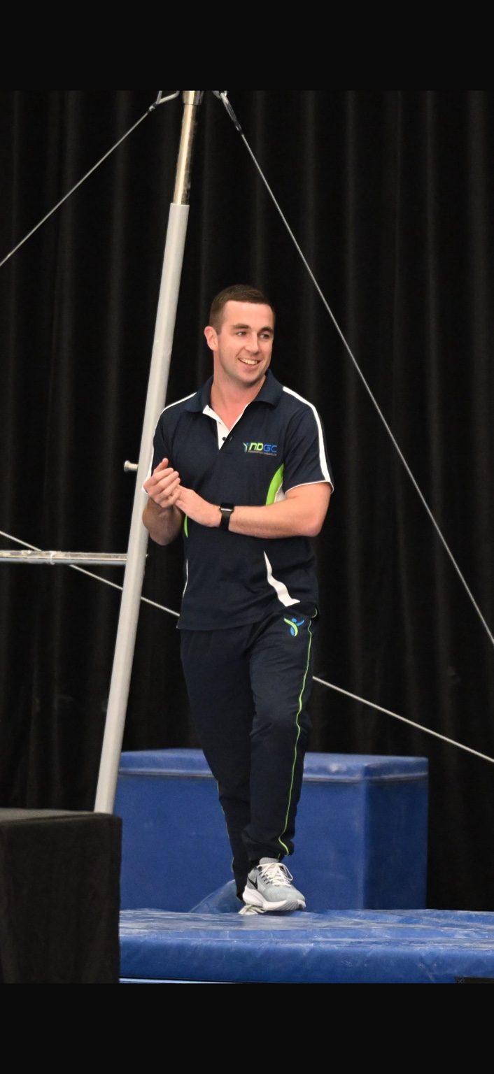 Ben Barnard smiling beside the uneven bars in a gymnastics training environment